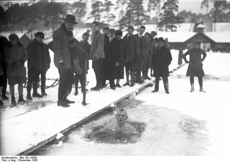 Ein Mann badet im Dezember 1930 in einem Eisloch in den Havelseen bei Berlin, am Rand stehen Zuschauer in Wintermänteln